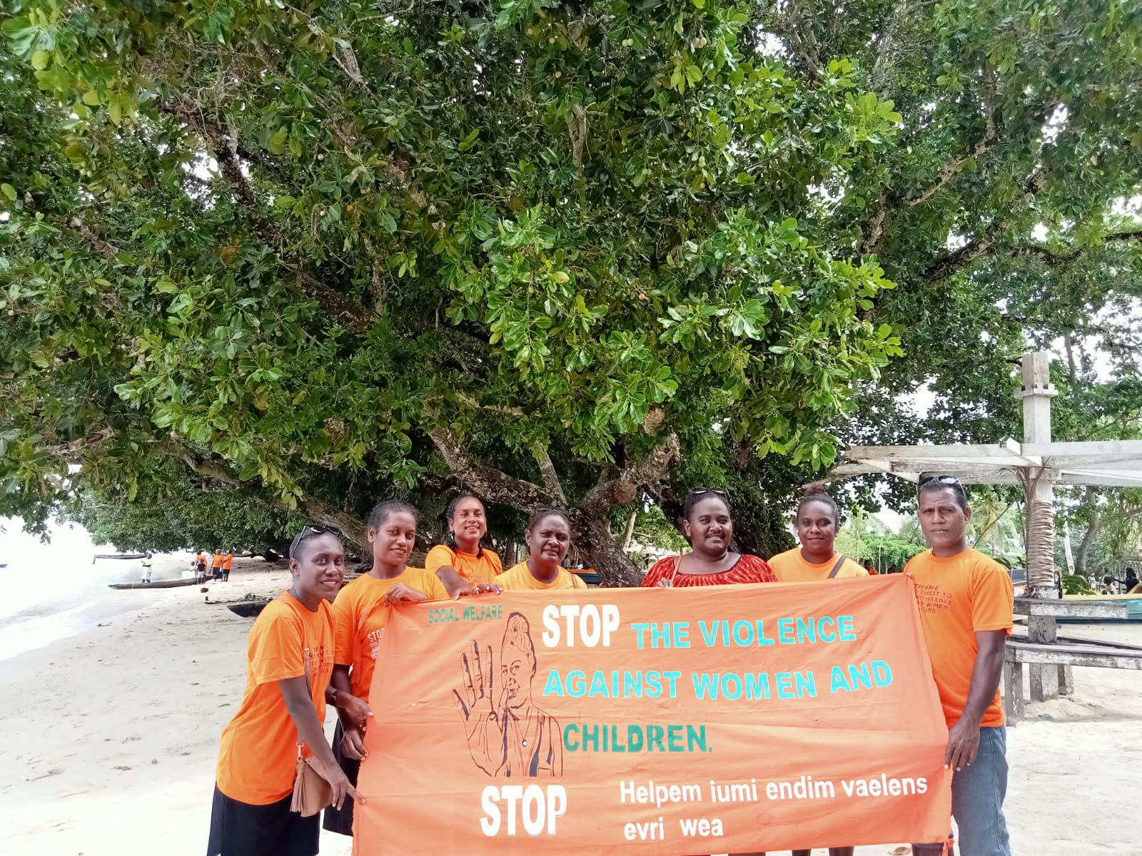 A group of people in orange t-shirts standing behind a banner that reads, "Stop the violence against women and children."