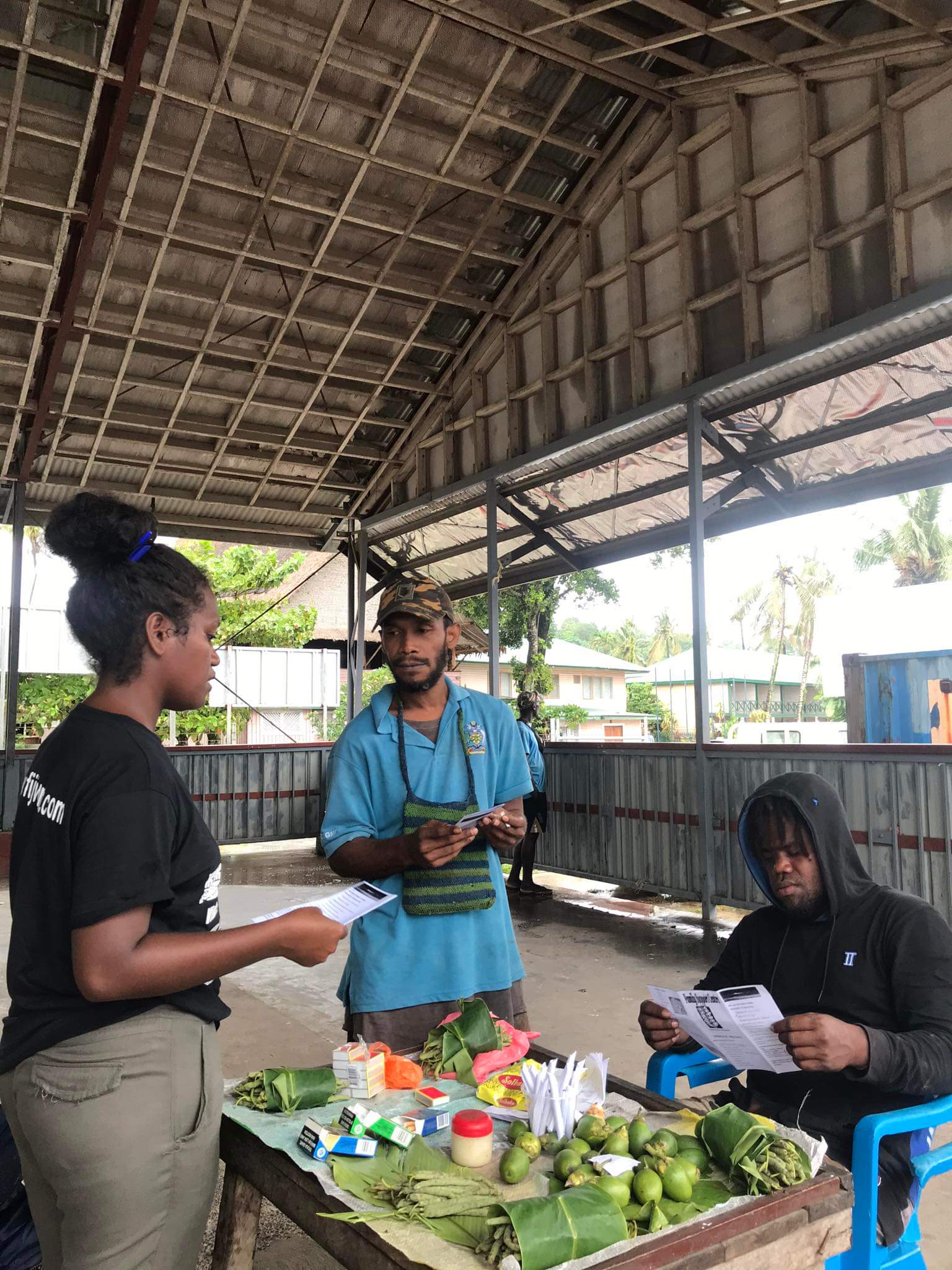 A Family Support Centre staff member talking to a group of men as she hands out pamphlets about gender-based violence to them.