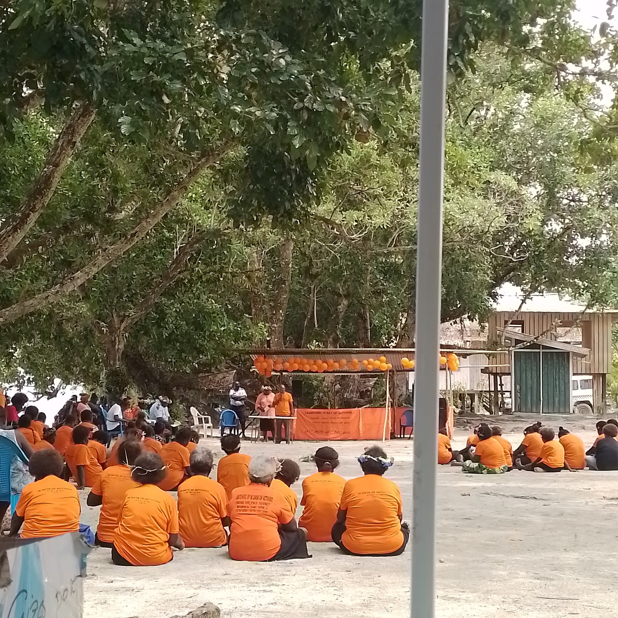 A group of people are sitting on the ground as they listen to a speaker.