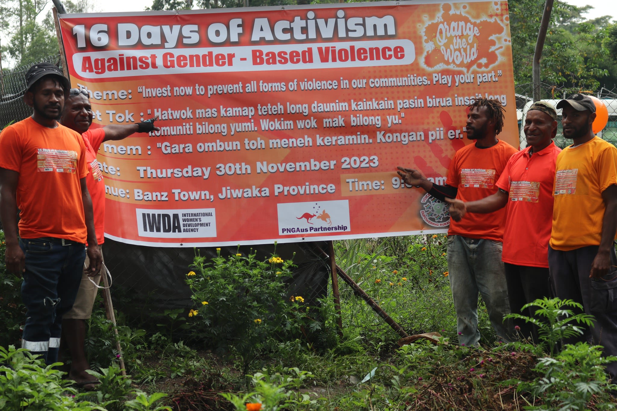 A group of men in orange t-shirts posing in front of a 16 Days banner.