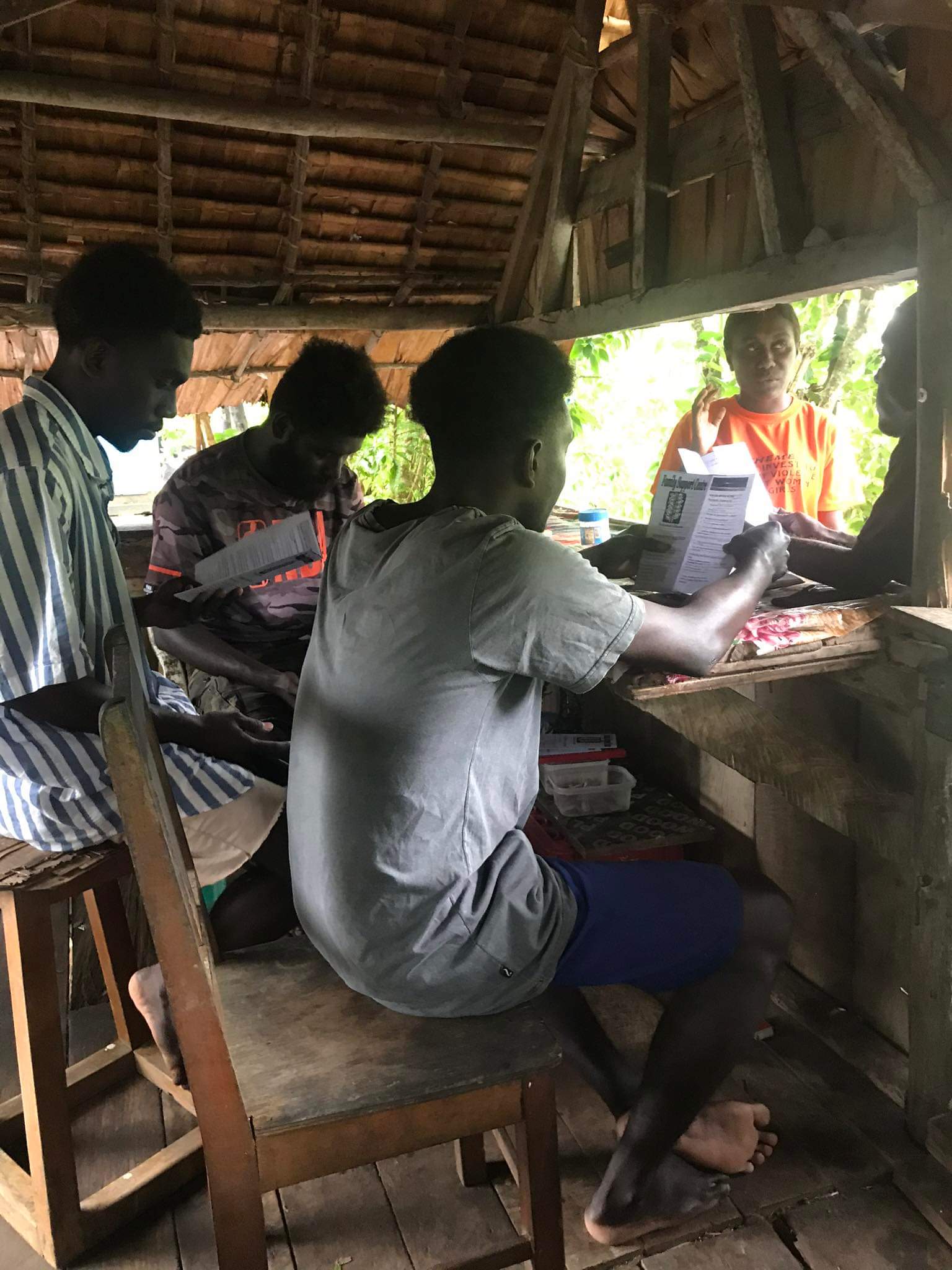 A Family Support Centre staff member talking to a group of men as she hands out pamphlets about gender-based violence to them.
