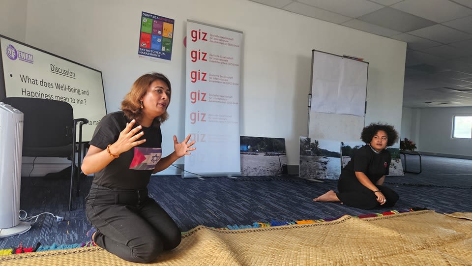 An FWRM staff member running the GIZ workshop. Behind them is a presentation that reads, "What does well-being and happiness mean to me?"