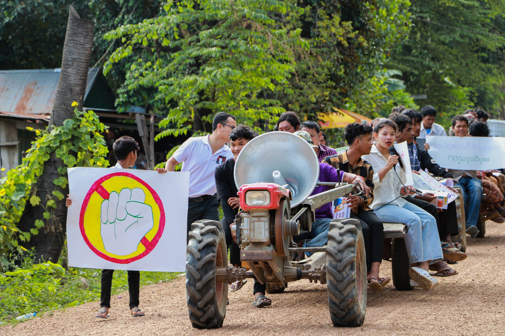 A group of people taking part in GADC's White Ribbon Day march. Some of them are riding on a tractor with a large megaphone attached at the front. One of them is holding up a sign with a drawing of a crossed-out fist in the centre.