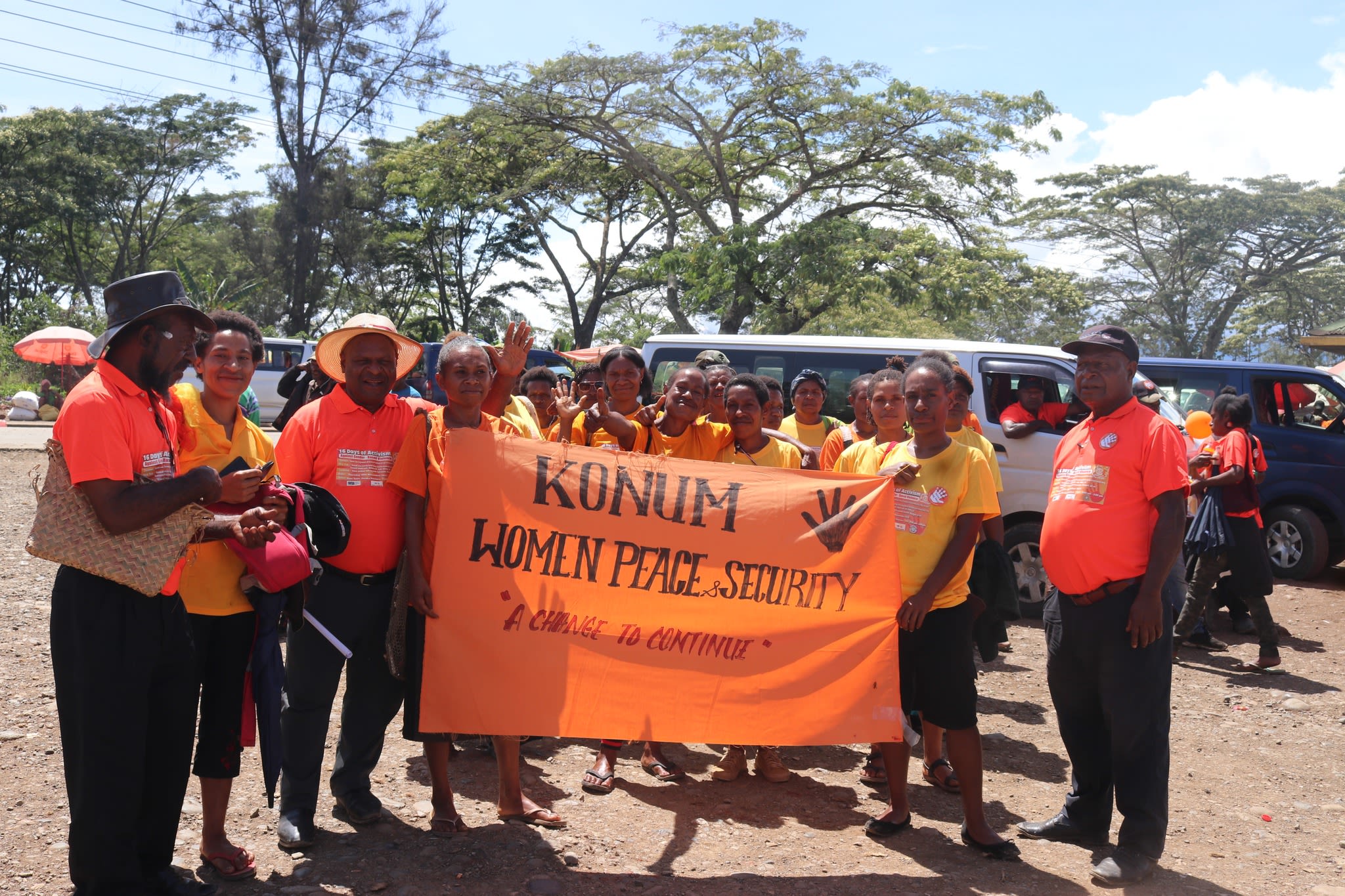 A group of people all wearing orange are posing with a banner that reads, "Konum. Women, peace and security. A change to continue."