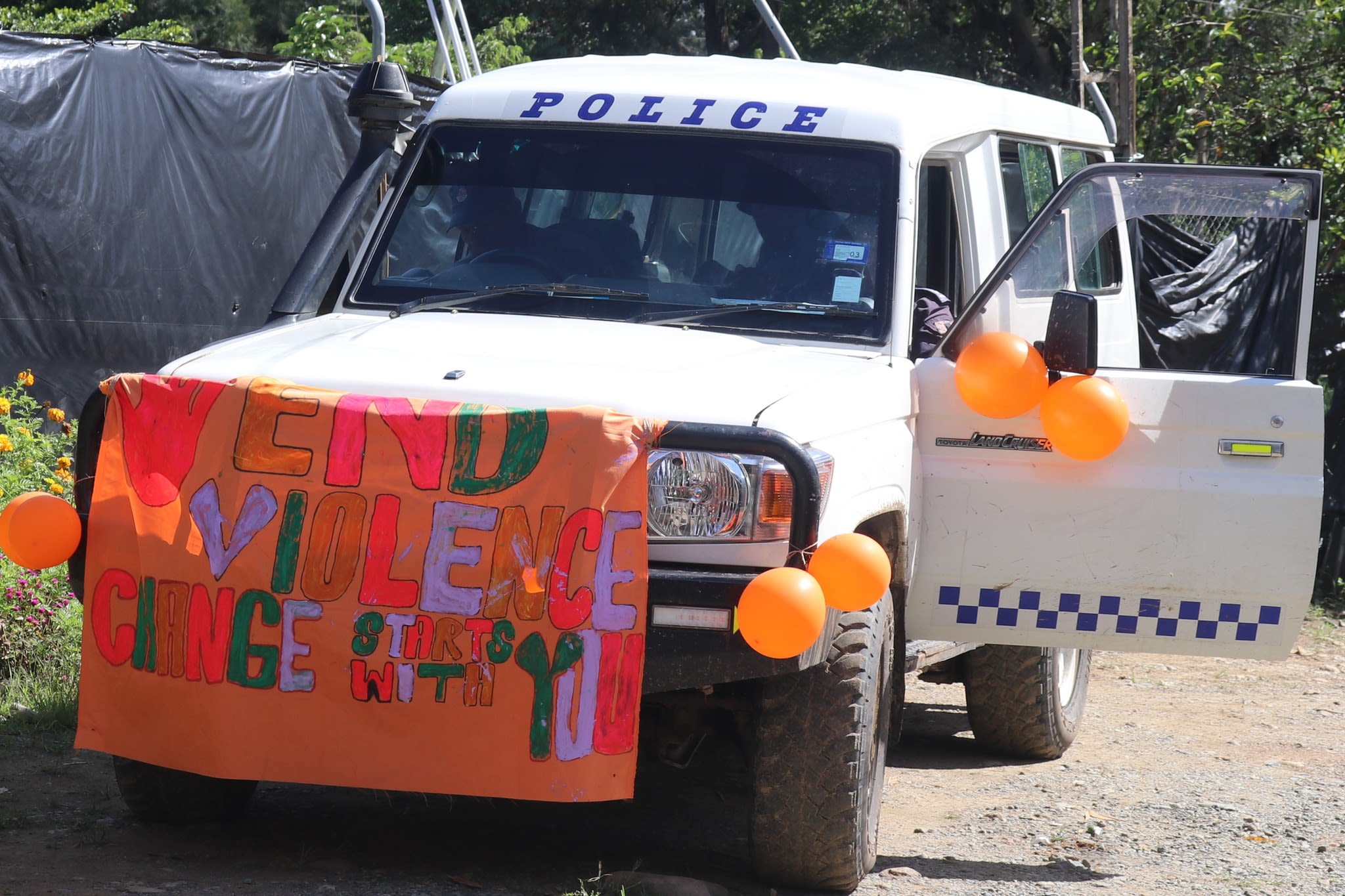 A police van decorated for the march with orange balloons and a banner that reads, "End violence. Change starts with you."