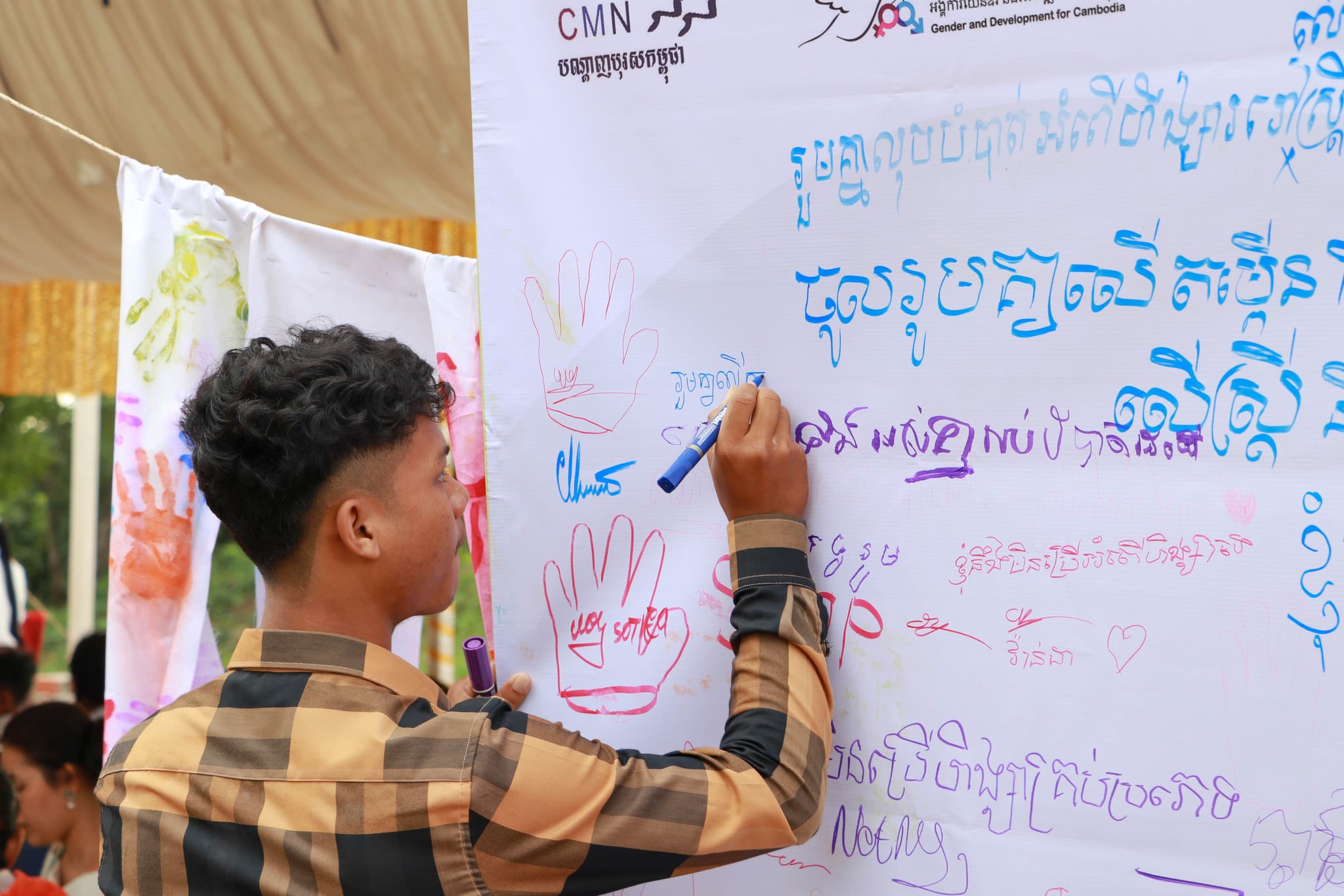 A young man is writing in Khmer on a sign at the White Ribbon Day event.