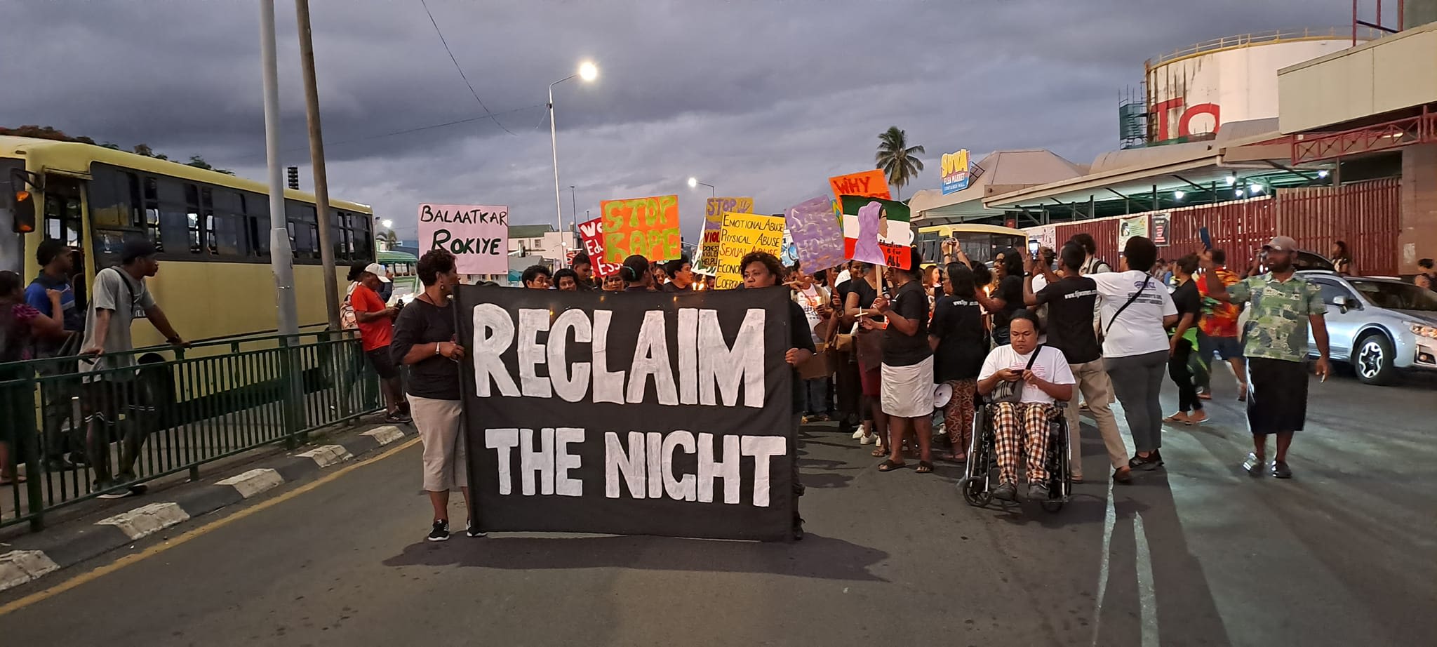 A group of people holding up signs while marching behind a black and white banner that reads, 'Reclaim the Night'