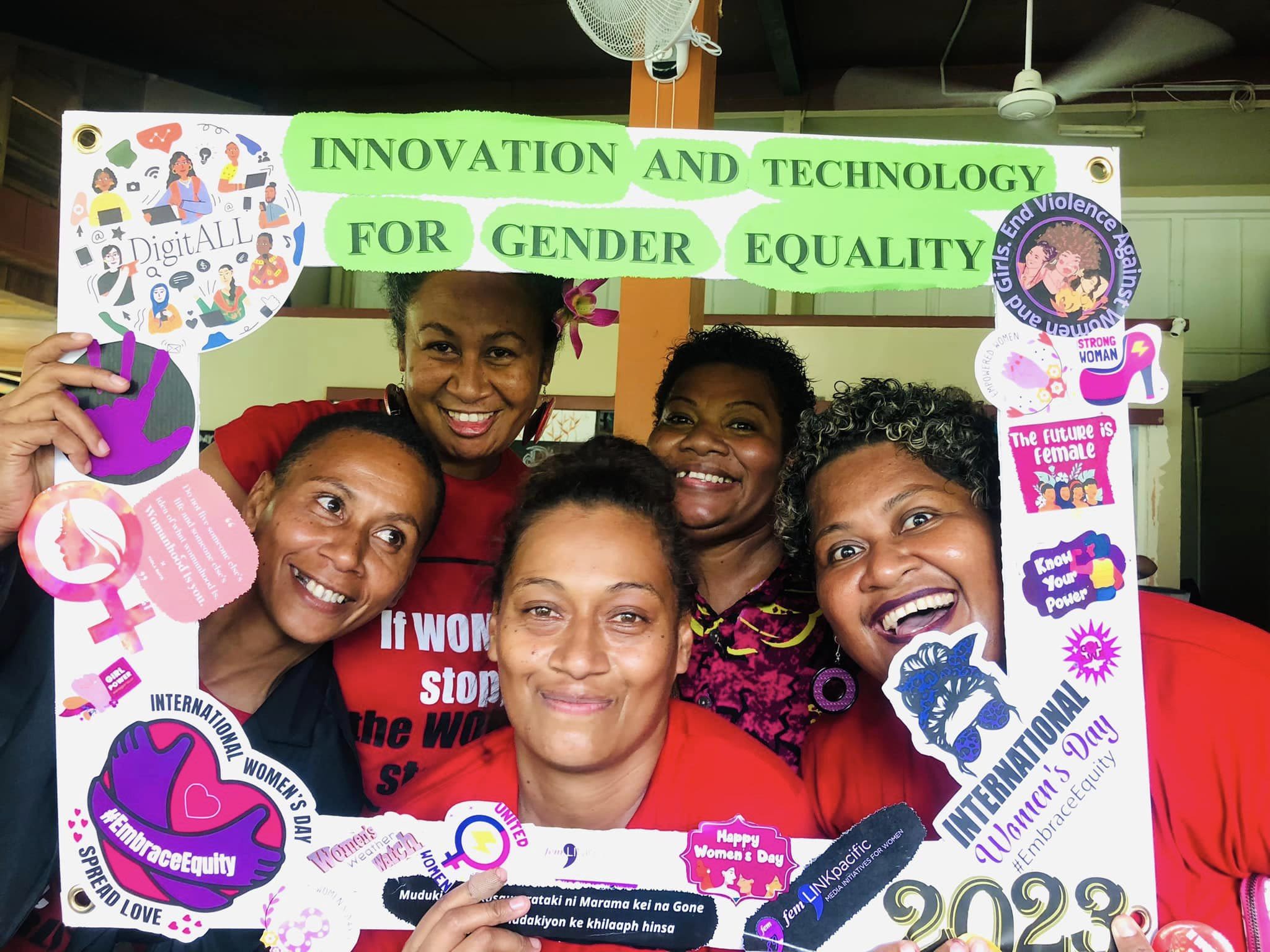 A group of five women posing with a selfie frame as they smile at the camera. The frame is full of slogans relating to International Women's Day and women's rights, including this year's theme 'Innovation and technology for gender equality.'