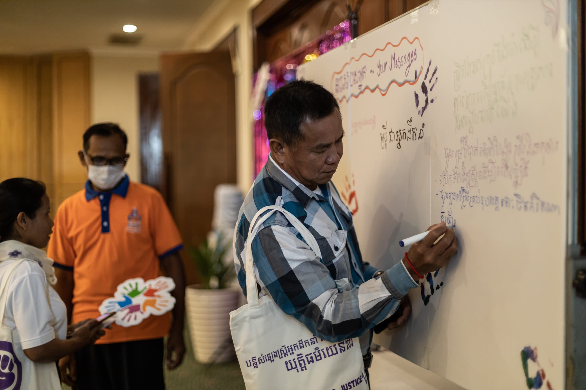 A man writing a message in Khmer on a whiteboard.