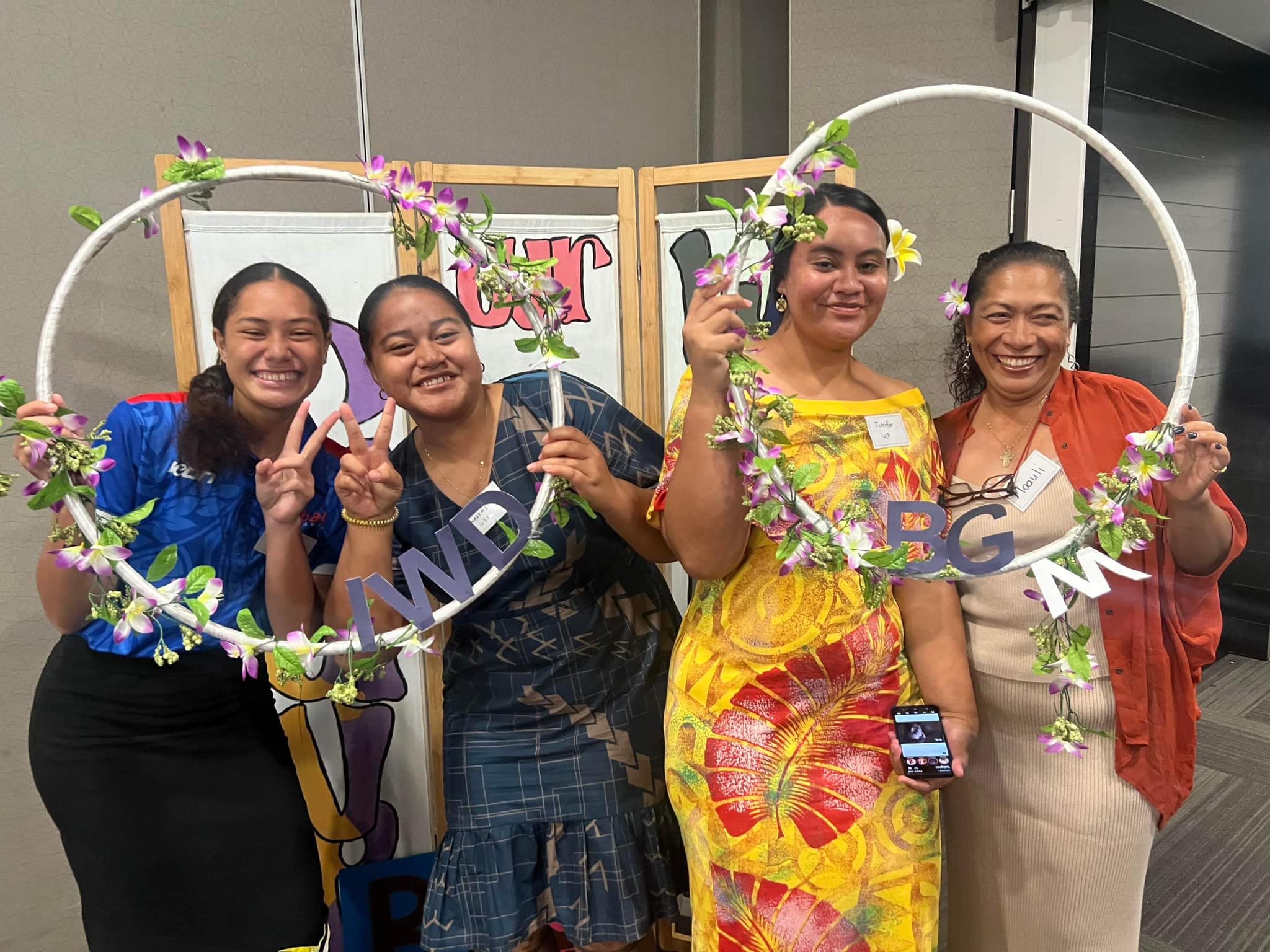 Four women smiling at the camera as they pose with selfie frames that read 'IWD' and 'BGW'