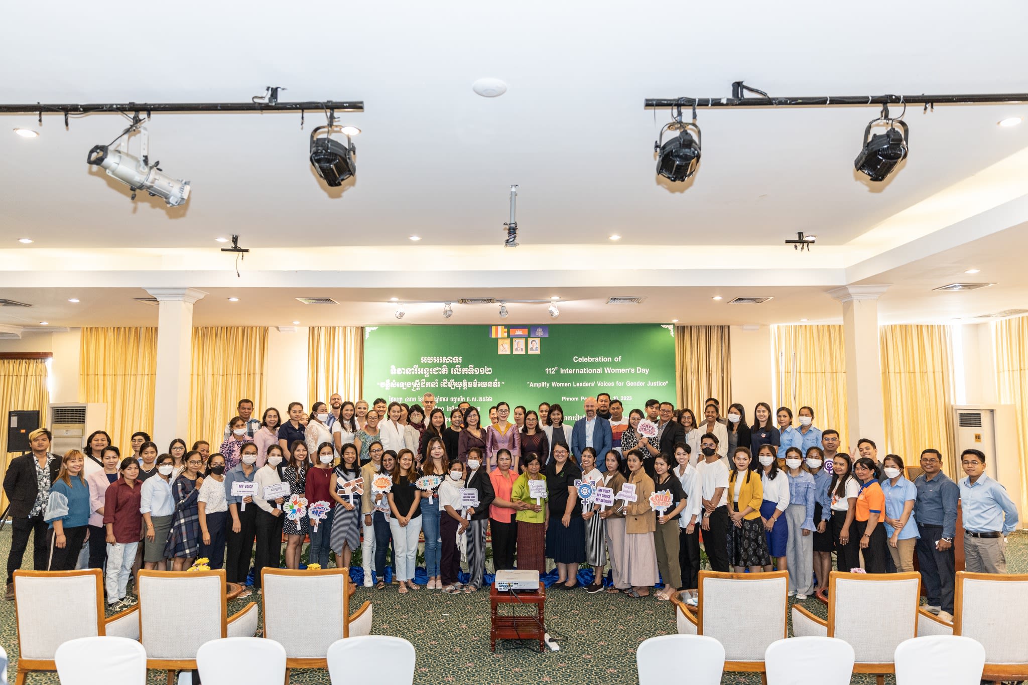 A large group of people in a conference room posing in front of the 'Amplify Women Leader's Voice for Gender Justice' forum banner