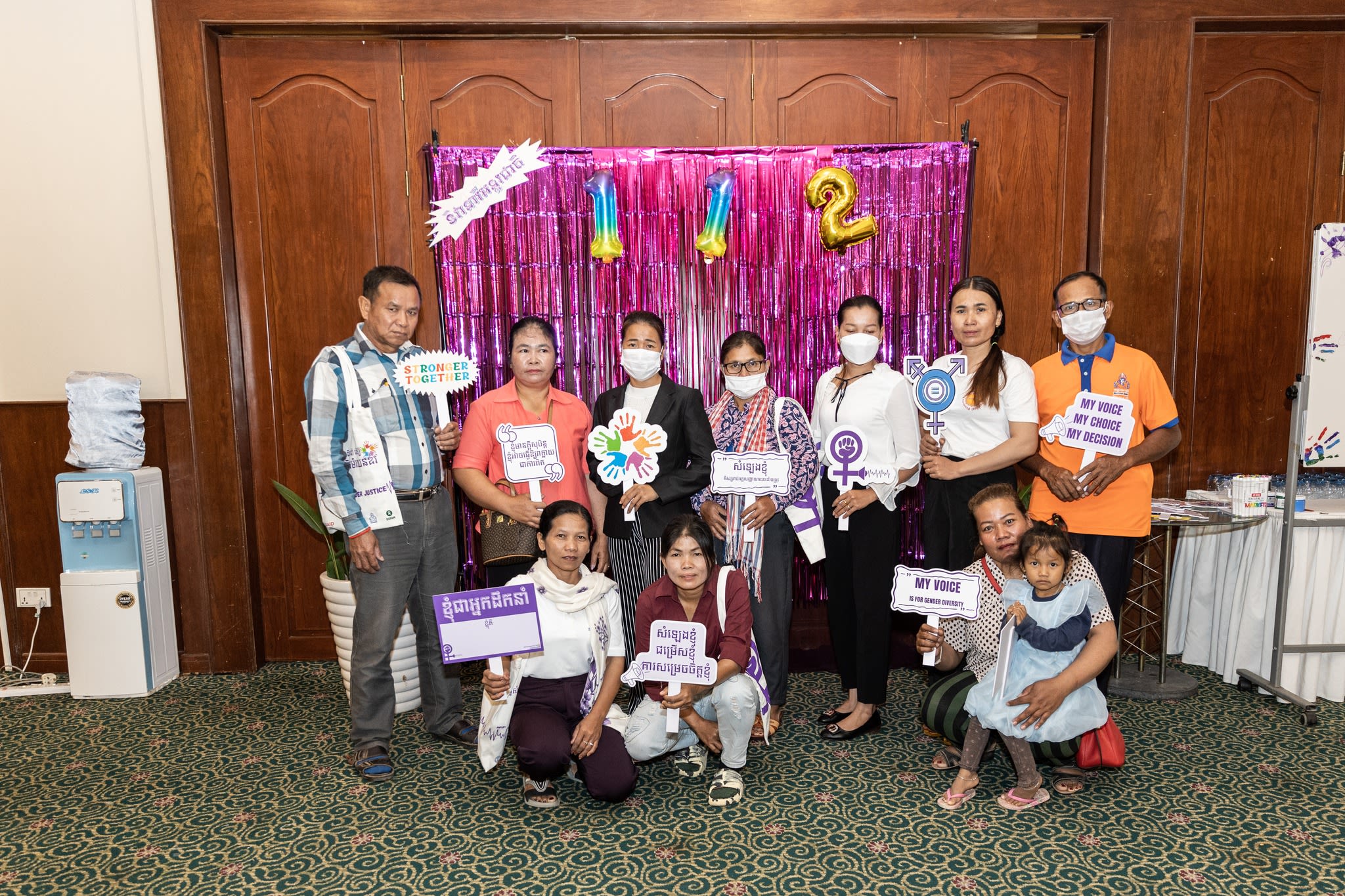 A group of forum participants posing together for a photo while holding up signs in Khmer
